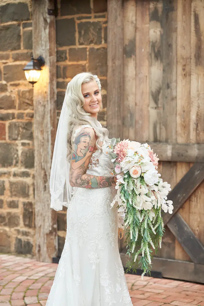 emma warrawong estate wedding bride bridesmaids portraits bouquet brick wall Portrait of bride Emma holding her wedding bouquet, standing slightly sideways and tilting her face toward the camera. A rustic brick wall and wooden door create a timeless backdrop at Warrawong Estate