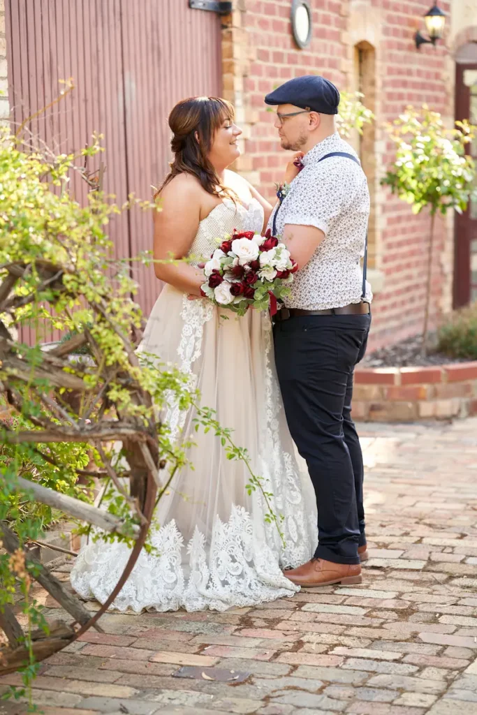 Bride and groom looking at each other with bouquet in front of red brick Bendigo Pottery building