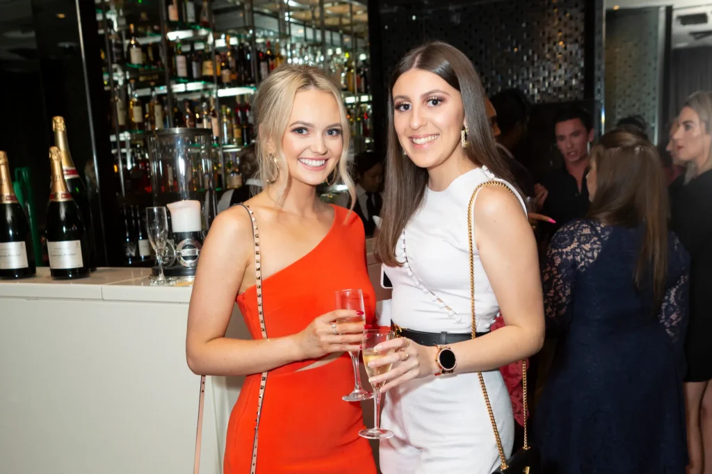 Two guests smiling and holding glasses of wine at a 21st birthday party