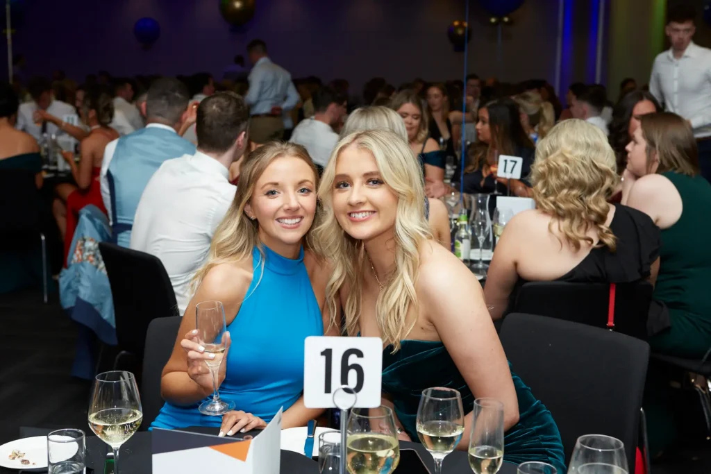 Two guests smiling at their banquet table during a Melbourne awards night and gala dinner, enjoying champagne and the evening celebration.