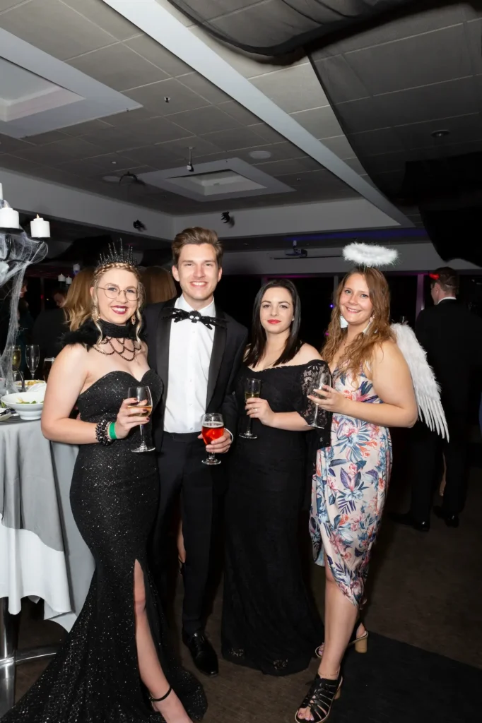 Four guests in formal attire with themed costume accessories pose together during a Melbourne awards night and gala dinner celebration.