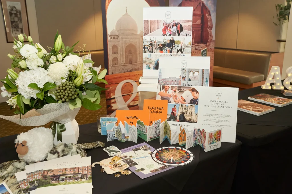 Vibrant luxury travel showcase display featuring colorful destination brochures, travel maps, promotional signage and a floral arrangement of white lilies, hydrangeas and roses, with a Taj Mahal backdrop at a Melbourne trade exhibition.