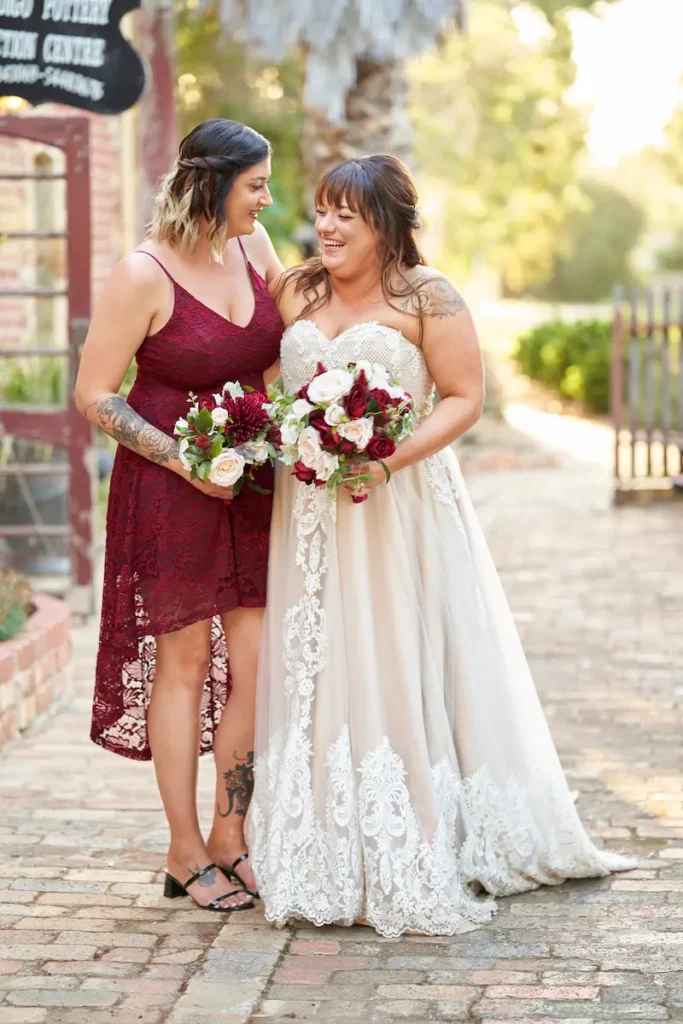 Bride and bridesmaids standing closely, laughing and holding bouquets with soft golden light in candid happy moment