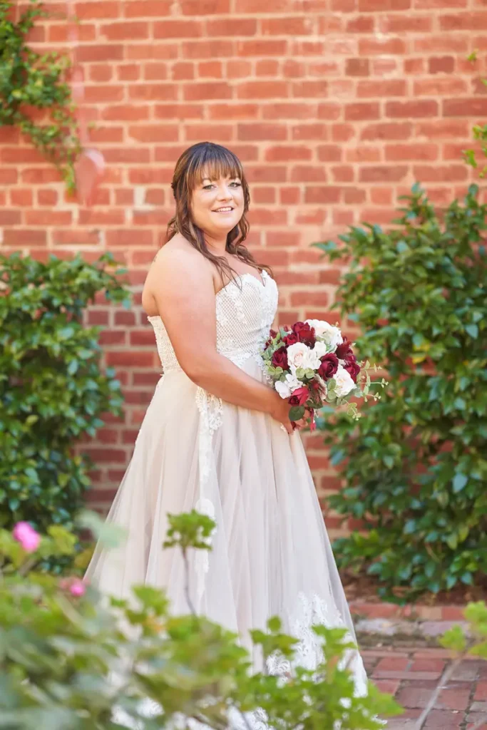 Bride holding a wedding bouquet with green plants and wall backdrop