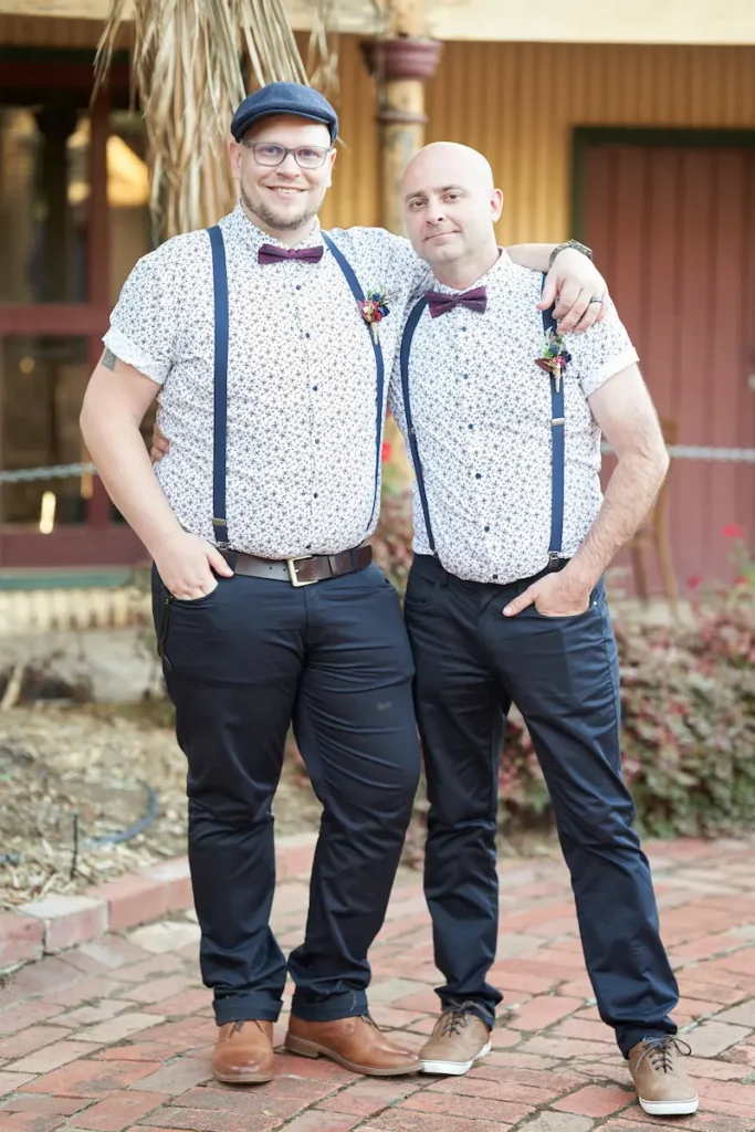 Groom and groomsman standing with hands in pockets, arms around each other’s shoulders in casual happy pose