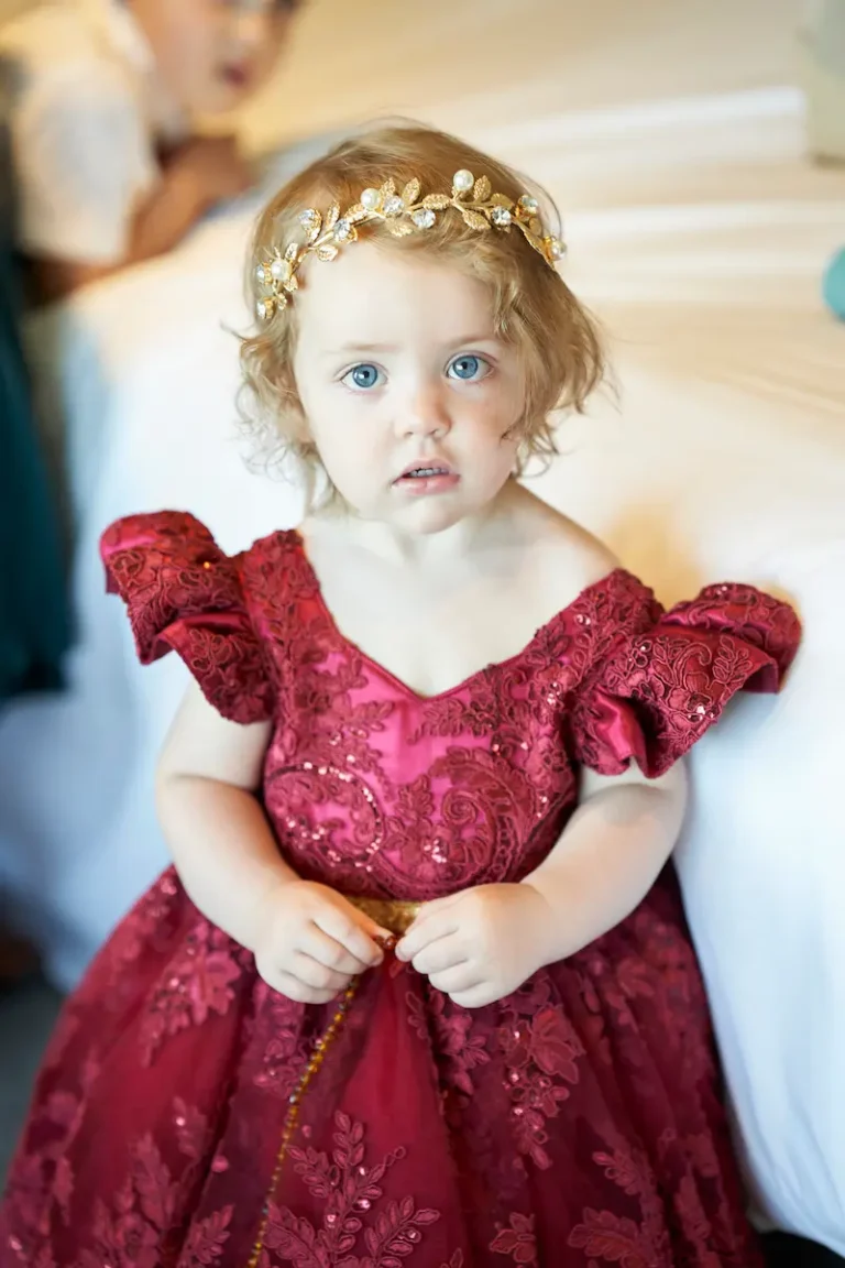 Portrait of super cute flower girl wearing red dress and gold leaf hair vines, looking like a fairy during bride getting ready