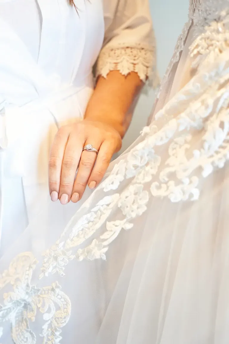 Close-up of bride’s hand wearing engagement ring near textured wedding dress fabric