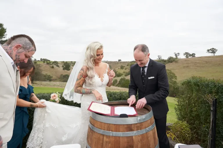 Bride Emma signing the wedding certificate on a wine barrel at Warrawong Estate, with the scenic valley, rolling hills, and cloudy skies in the background