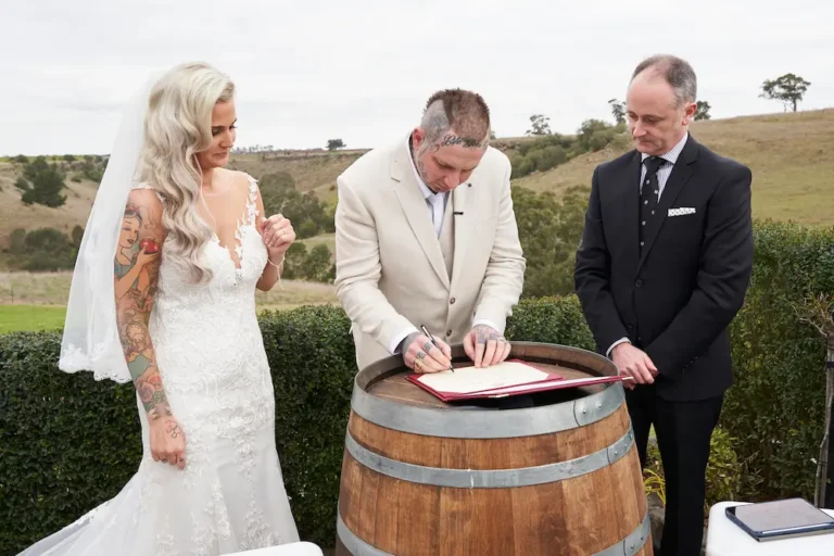 Groom Darko signing the wedding certificate on a wine barrel at Warrawong Estate, with the scenic valley, rolling landscape, and overcast skies in the background