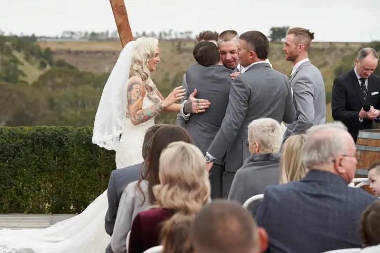 Groomsman hugging groom Darko to congratulate him after the wedding ceremony at Warrawong Estate, with the scenic valley, rolling landscape, and overcast skies in the background