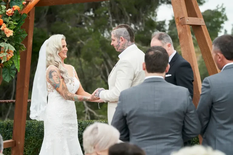 Bride Emma and groom Darko holding hands and facing each other, smiling during their Warrawong Estate wedding ceremony, with a large tree visible in the background