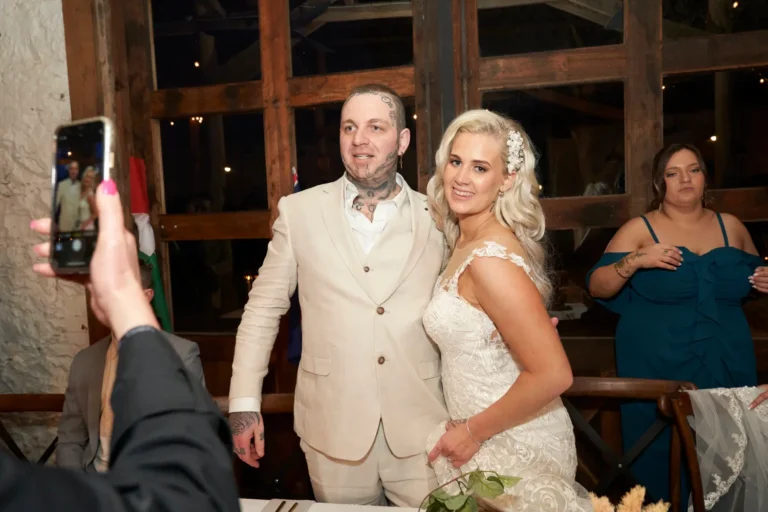 Candid photo of bride and groom standing at the reception table at Warrawong Estate, smiling at the camera while guests take pictures of her on their phones