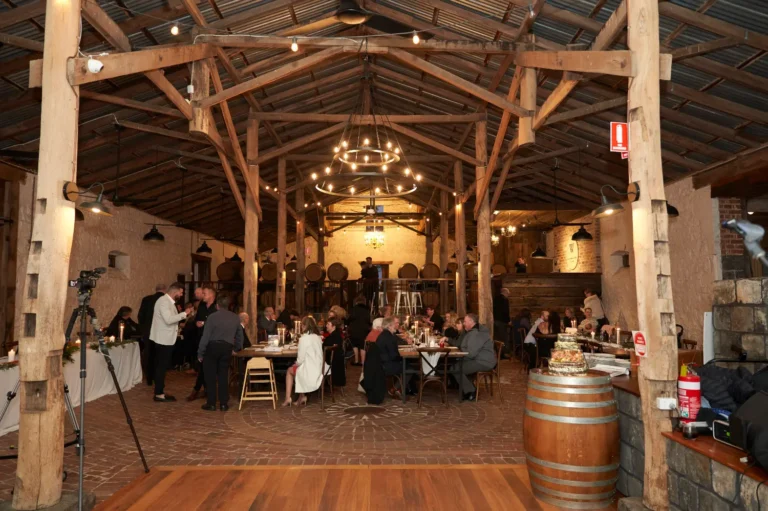 Wide shot of Emma and Darko’s wedding reception at Warrawong Estate, showing guests seated at tables and the softly illuminated room with chandeliers, capturing the elegant atmosphere