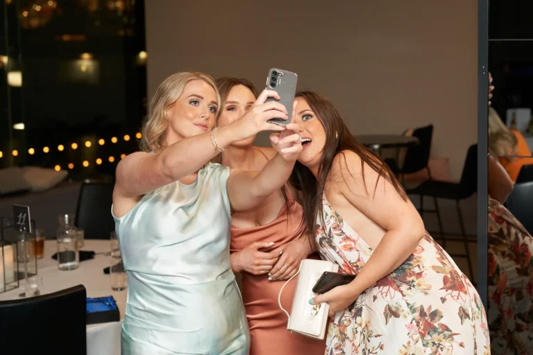 garryowen awards night rivers edge candid three women selfie Three women at the Garryowen Awards Night at River’s Edge Events taking a selfie, including a woman in a light-colored dress holding the phone, a woman in a floral dress smiling widely, and a woman in a satin dress looking at the camera