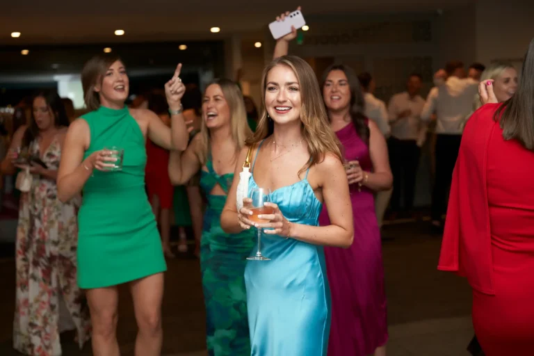 garryowen awards night rivers edge women celebrating dance floor A group of well-dressed women socializing and celebrating on the dance floor, with a woman in a light blue satin dress holding a pink drink, at the Garryowen Awards Night at River’s Edge Events, while other guests dance and laugh in the background