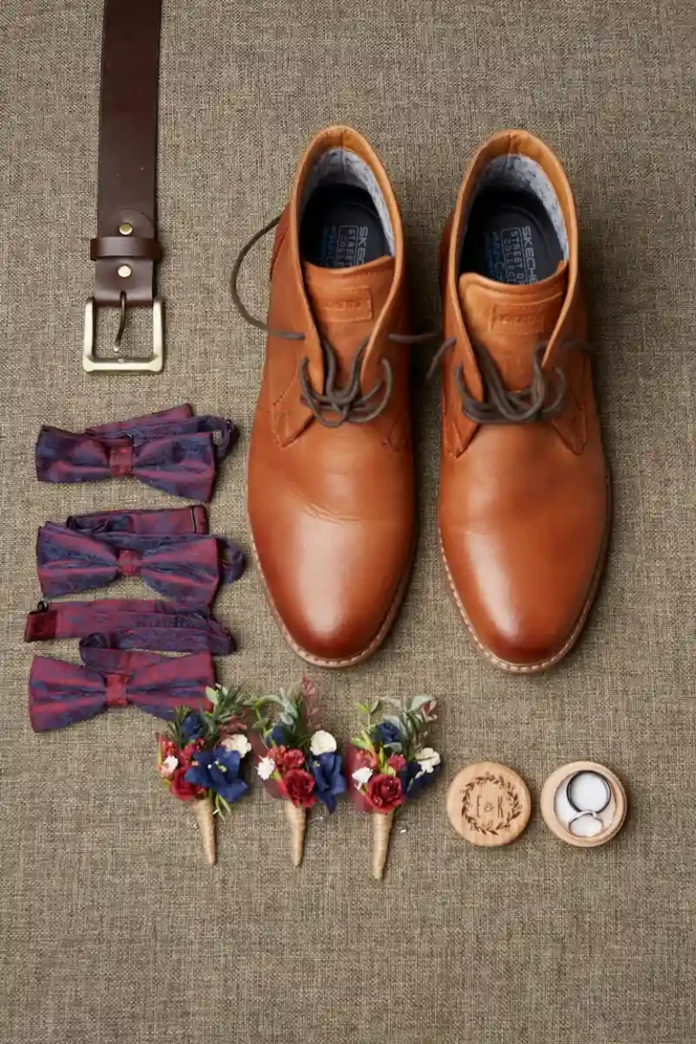 Styling shot of boutonnière, wedding rings, bow tie, shoes, and belt during groom’s preparation