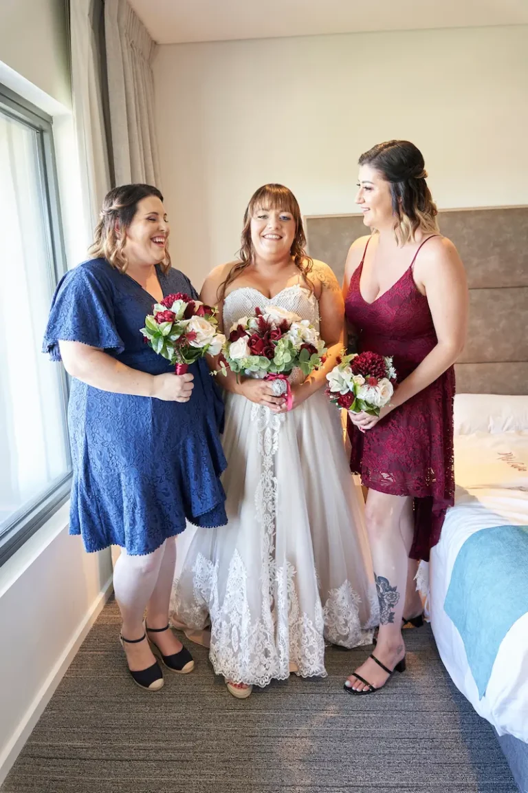 Bride and bridesmaids after dressing, smiling and laughing candidly while holding bouquets during bride getting ready indoors