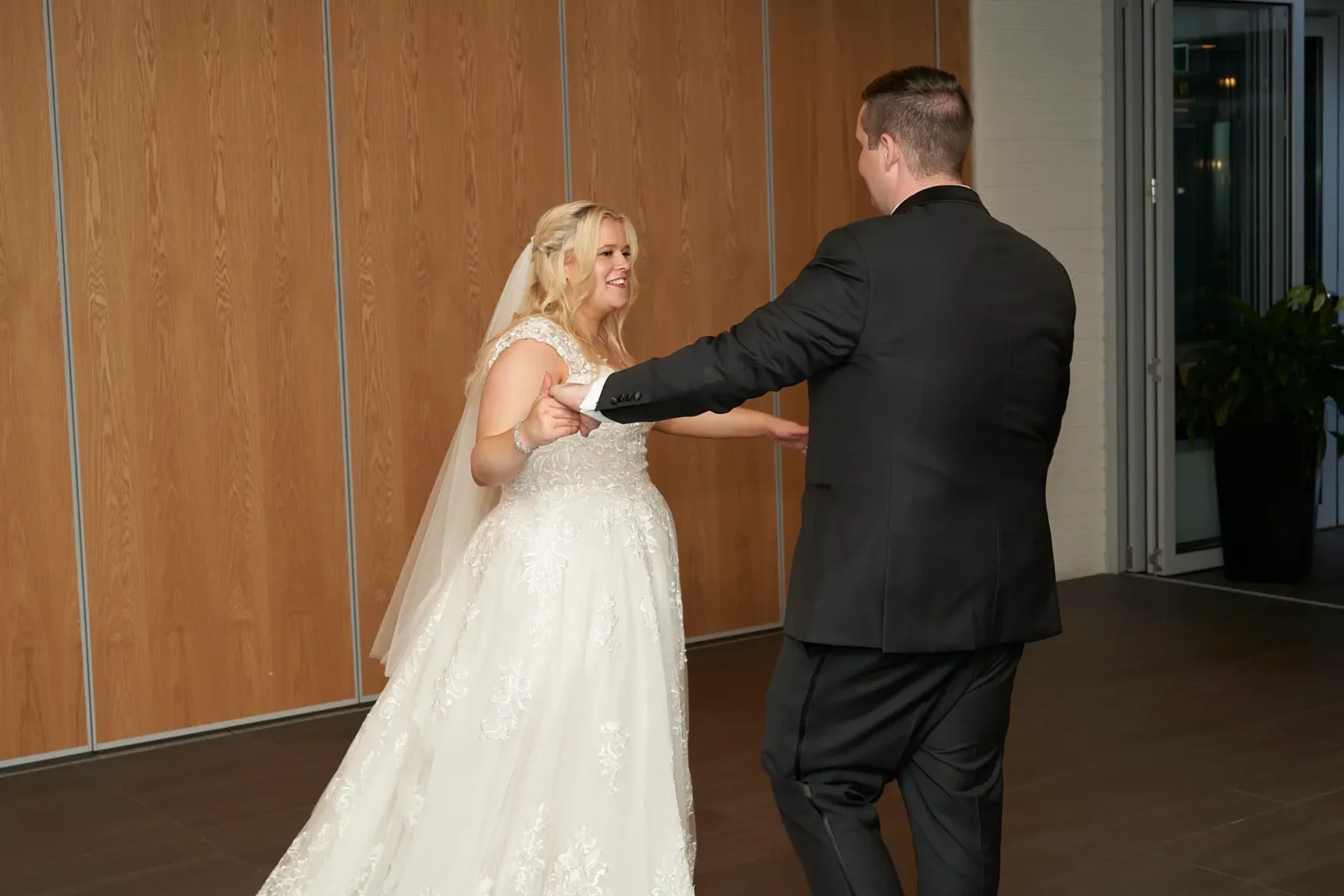 Bride and groom share a joyful first dance at their wedding reception at Amora Herencia Riverwalk Melbourne. Holding hands, the groom gently twirls the bride in her lace A-line wedding gown and veil as they smile at each other on the dance floor, capturing a playful and romantic moment during their intimate Melbourne wedding celebration.
